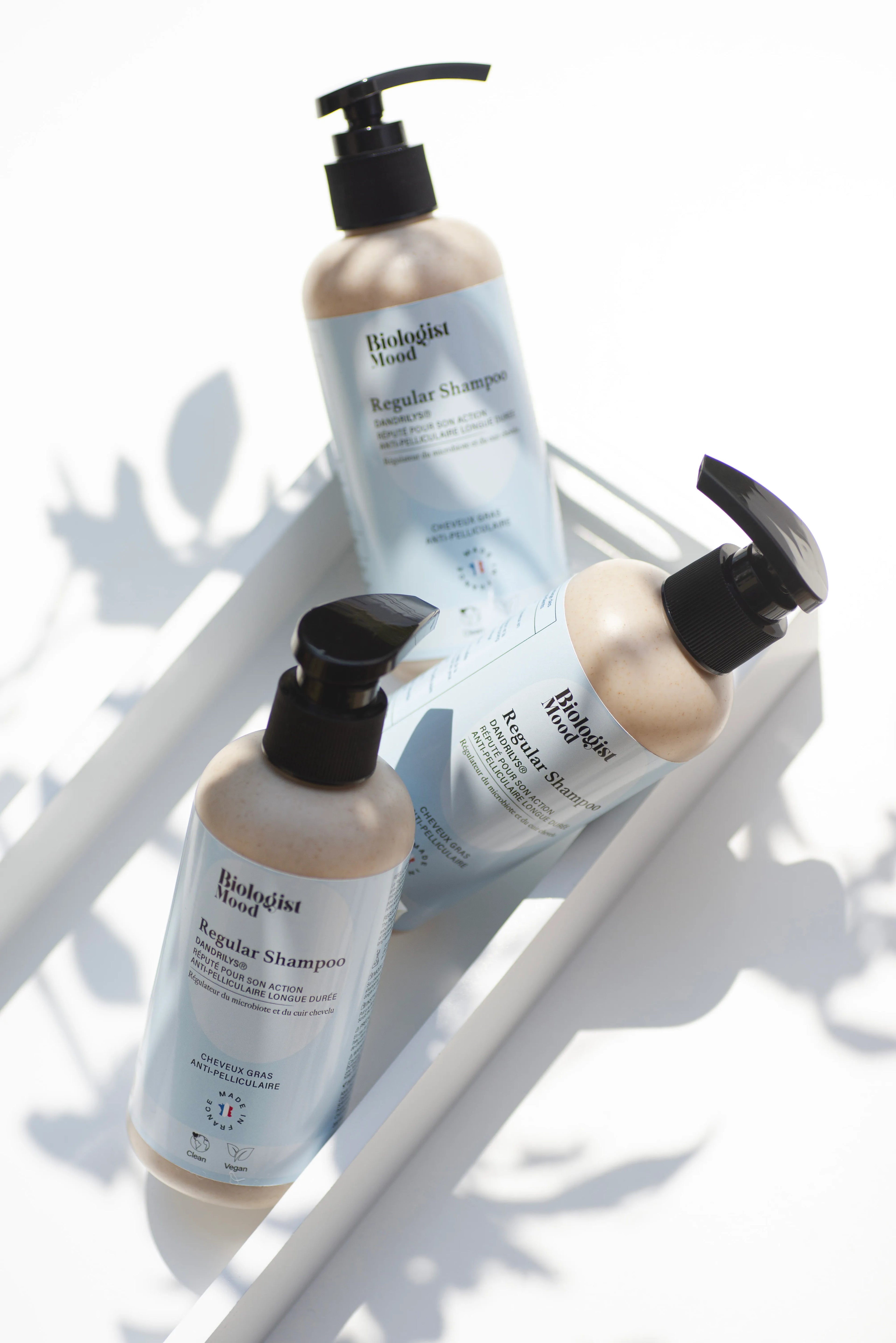 rois flacons de shampoing sans sulfate posés dans un plateau blanc, lumière naturelle