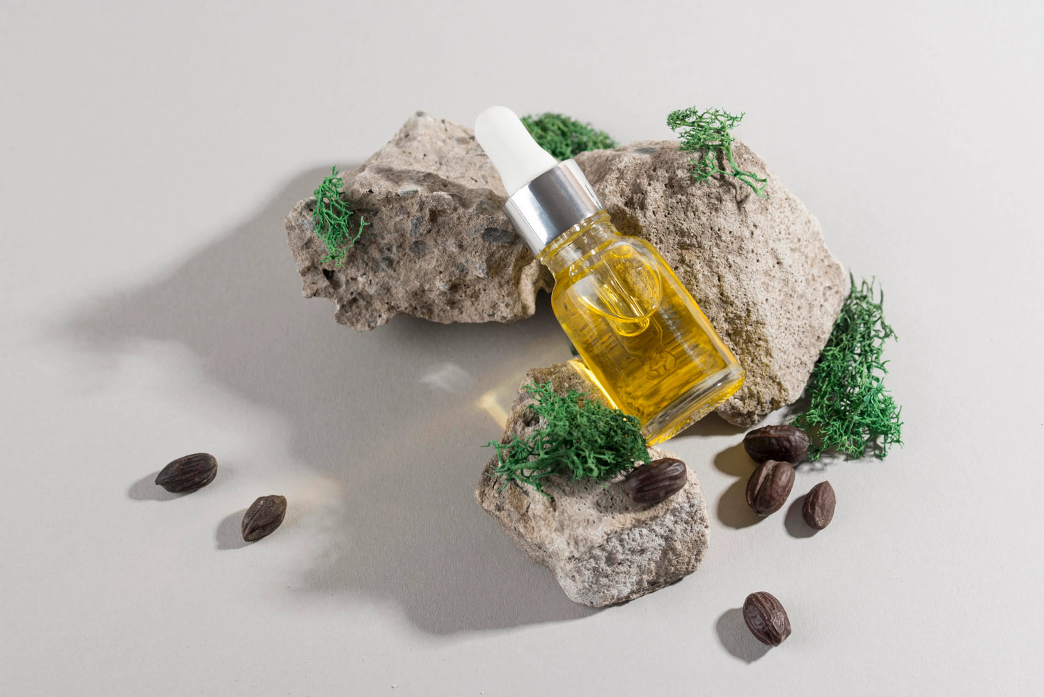 Dropper bottle of natural jojoba oil placed on rocks with green plants and seeds, illustrating a hair growth oil treatment for healthy hair