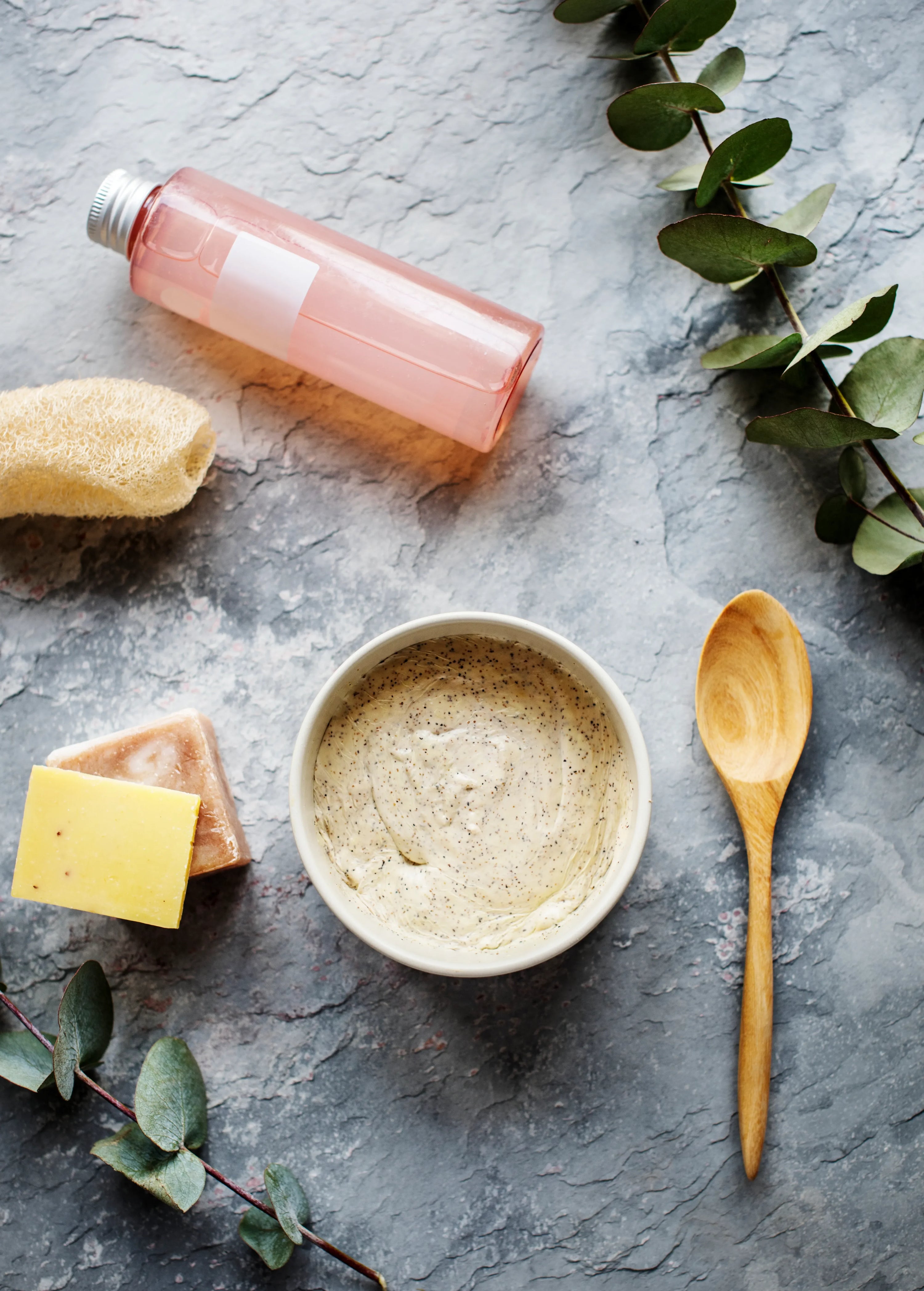 Flatlay de produits capillaires naturels avec huiles, gommage et accessoires spa sur fond clair, routine douce pour cheveux colorés