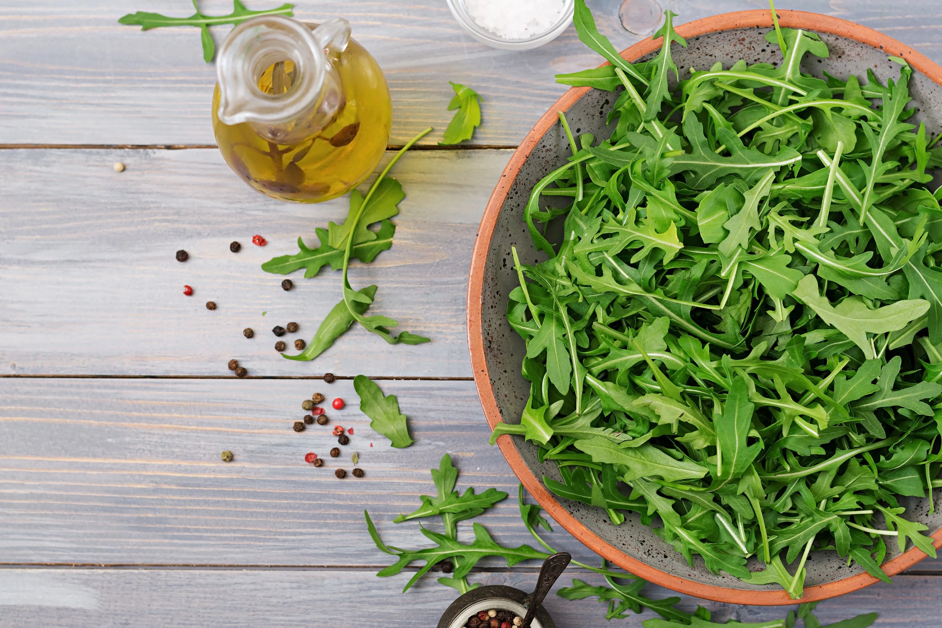 Fresh arugula leaves in a wooden bowl with a bottle of natural oil, illustrating arugula oil used as a natural remedy to stimulate hair growth and strengthen hair