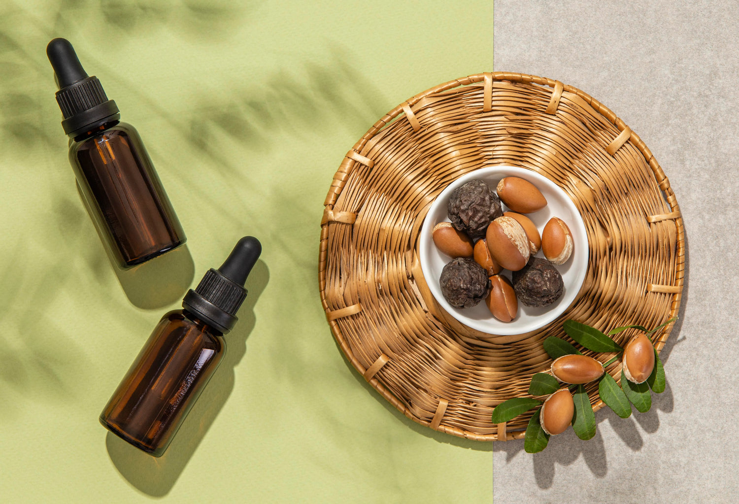 Vue de dessus de flacons d’huile capillaire naturelle avec pipette, posés à côté d’un bol contenant des graines (type ricin) sur un fond vert, illustrant des huiles pour la pousse des cheveux