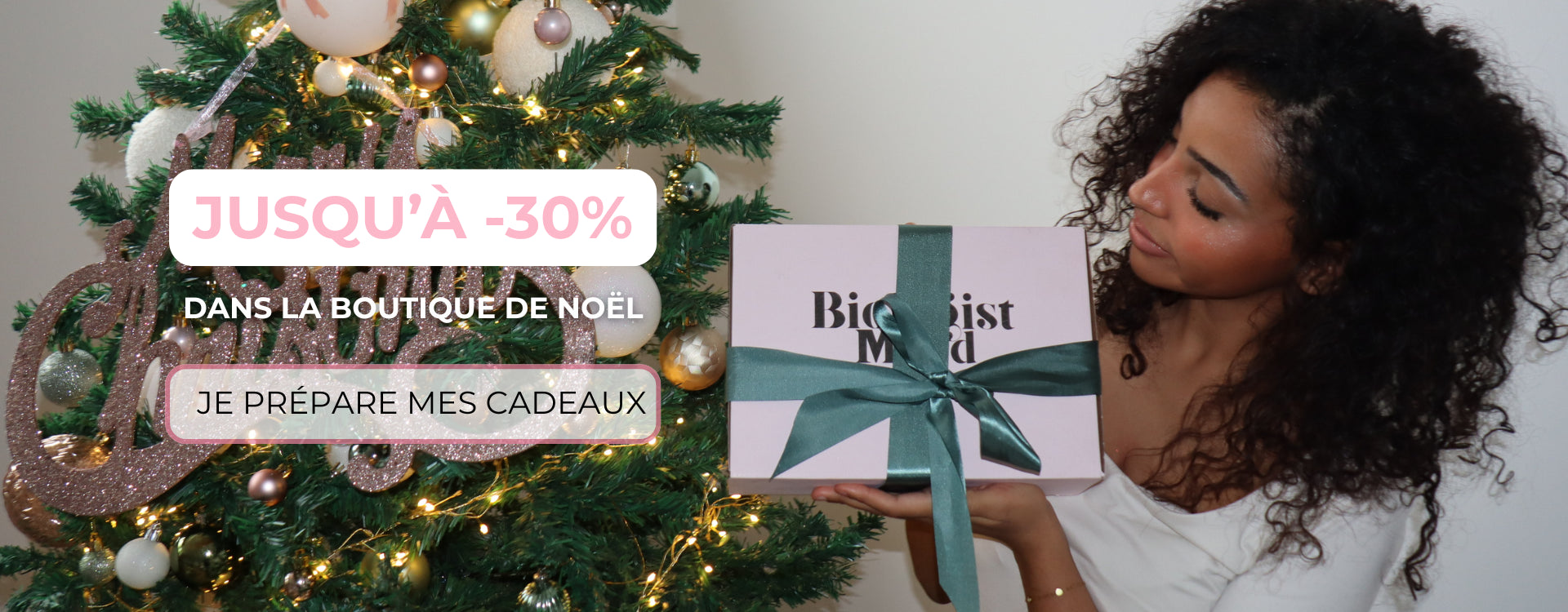 Femme offrant un cadeau de Noël devant un sapin décoré, promotion jusqu’à -30 % sur la boutique Biologist Mood.