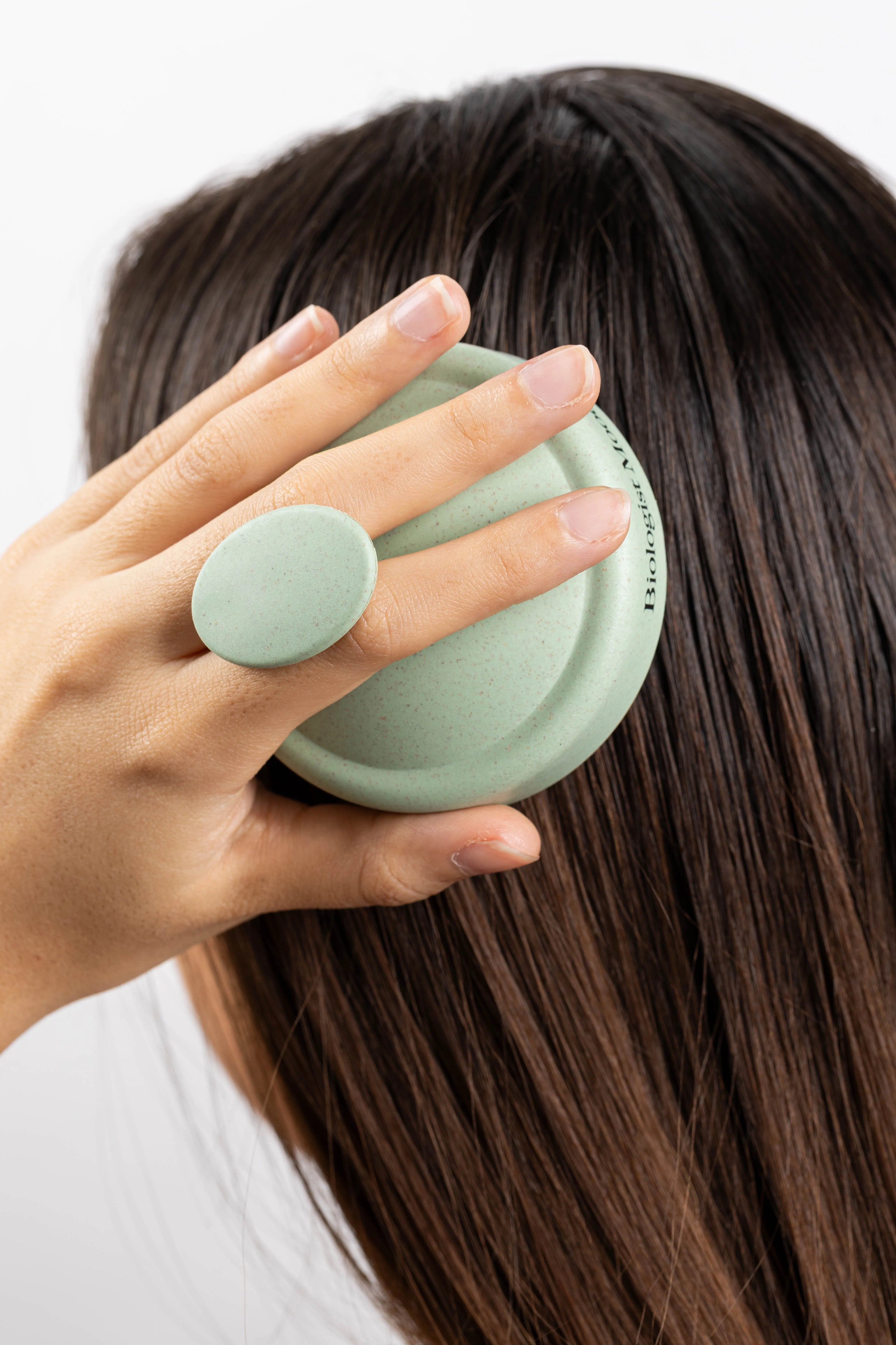Main tenant une brosse stimulante Biologist Mood sur des cheveux bruns, utilisée pour masser le cuir chevelu et favoriser la pousse des cheveux