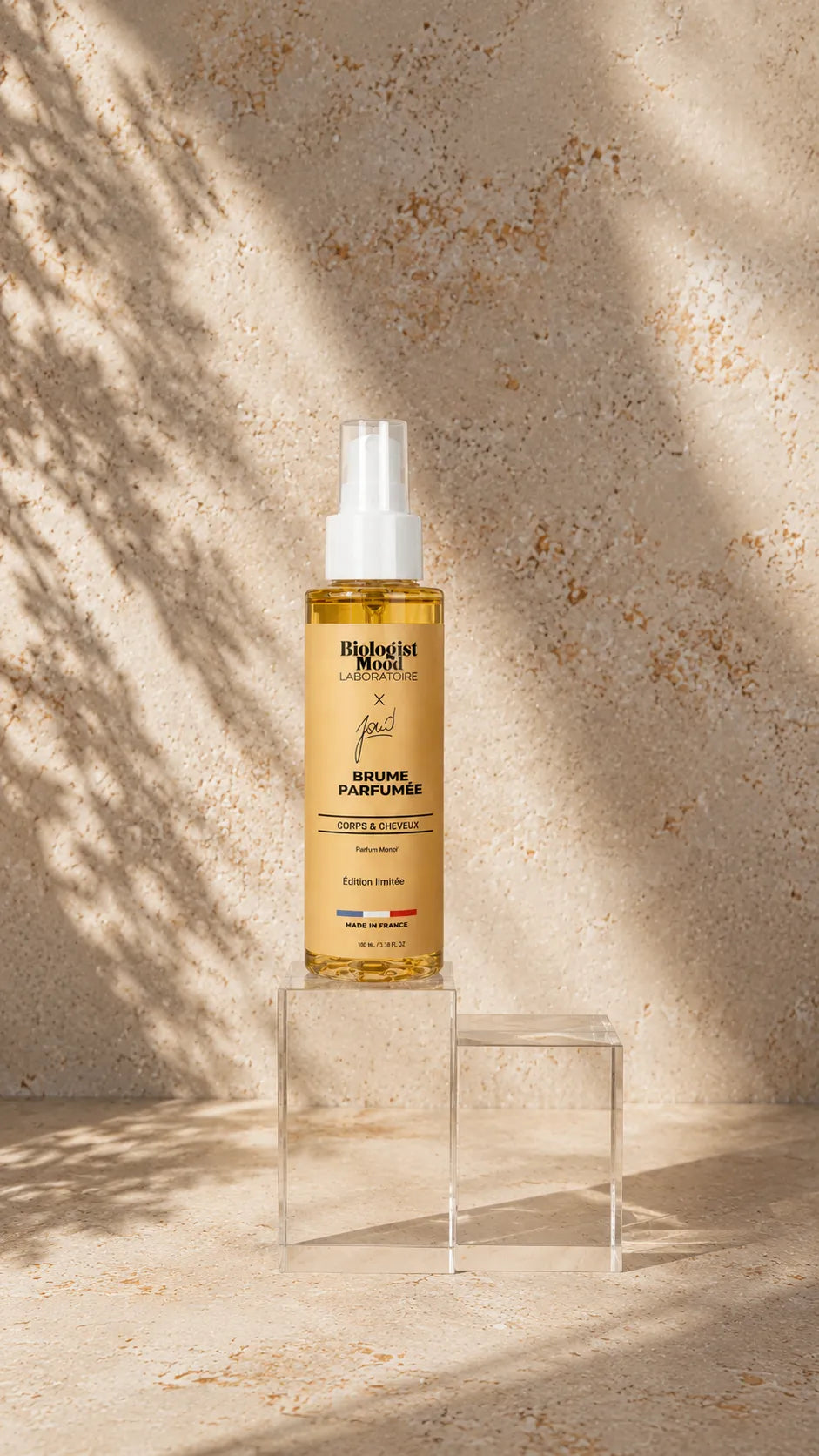 Brume parfumée Biologist Mood pour cheveux et corps aux notes de monoï, flacon spray premium sur fond beige naturel, parfum d'été hydratant et rafraîchissant.