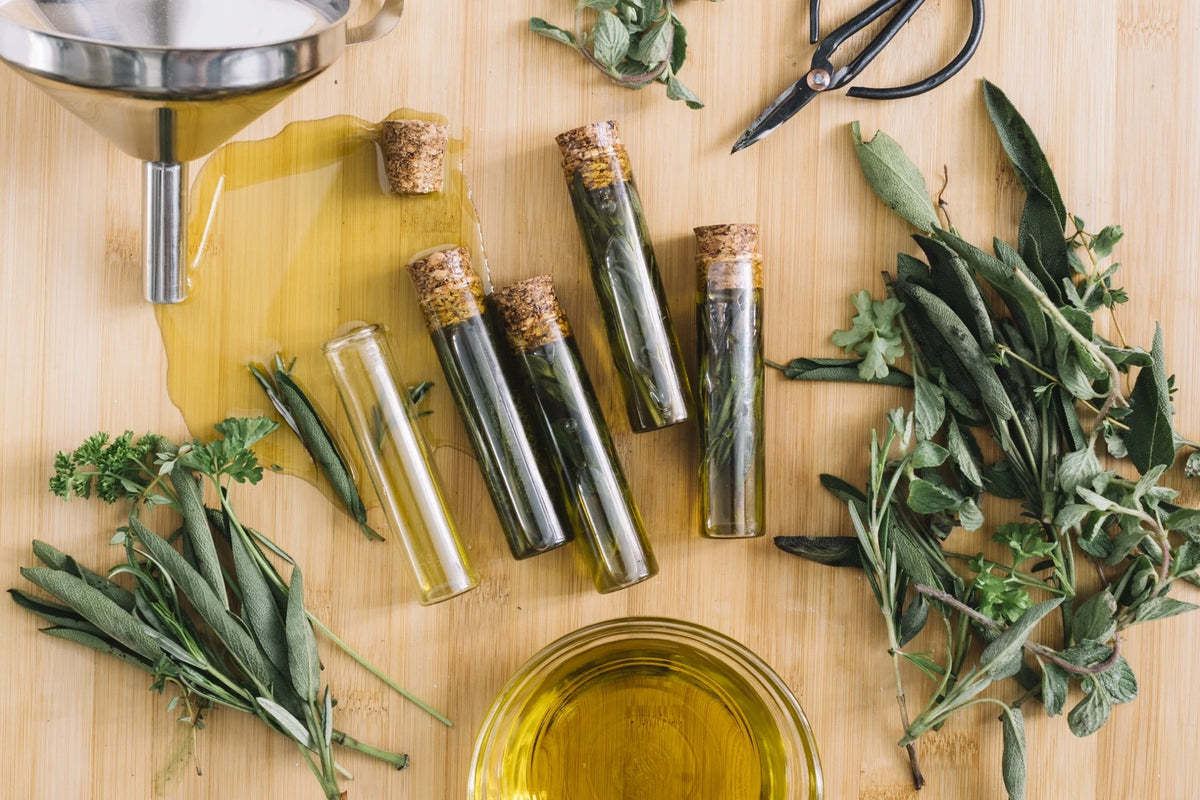 préparation d’huiles végétales naturelles avec des herbes fraîches — romarin, sauge et persil — sur une table en bois, pour créer des soins capillaires faits maison.