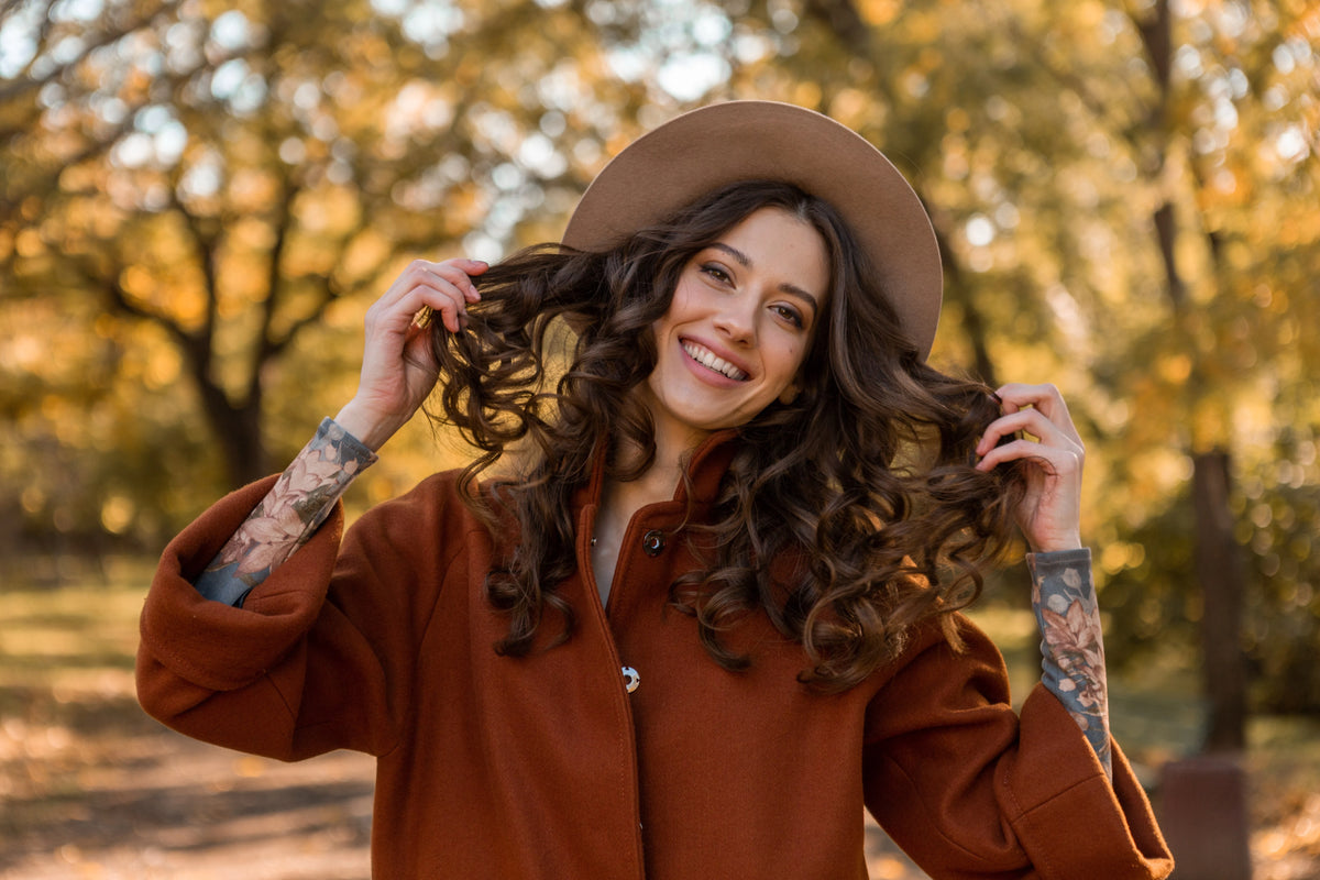 Femme souriante aux cheveux bouclés profitant de l’automne, symbole de vitalité et de pousse capillaire naturelle grâce aux compléments Biologist Mood