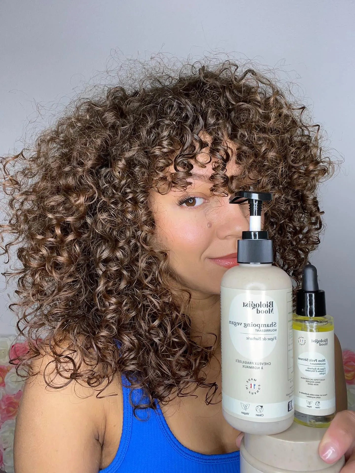 Modèle aux cheveux bouclés tenant le shampoing nourrissant &amp; hydratant à la figue de Barbarie – soin vegan pour cheveux secs Biologist Mood.